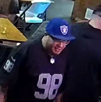 Help identify this suspect wearing a blue baseball cap, dark colored shirt that has the numbers \